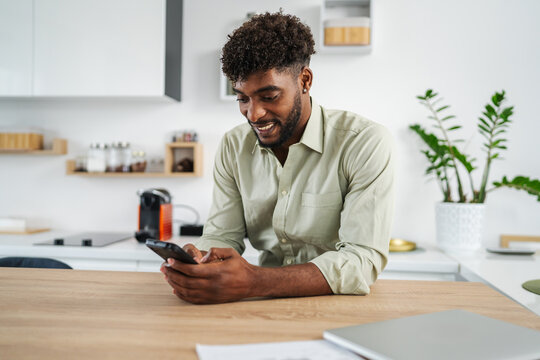 Young black man smiling using smart phone in kitchen