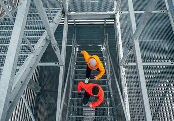 Top view of Two bright red and yellow sporty clothes dressed men running up on huge steel industrial stairs in cold winter day. Men's friendship and healthy lifestyle concept photo.