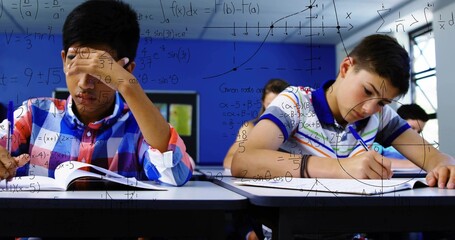 Solving math two students plaid, striped polos at class desks, writing in workbook, math overlay