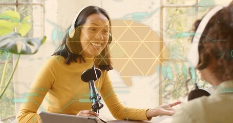 Talking host in mustard top with headset speaking into mic at bright table, laptop, overlays, plant