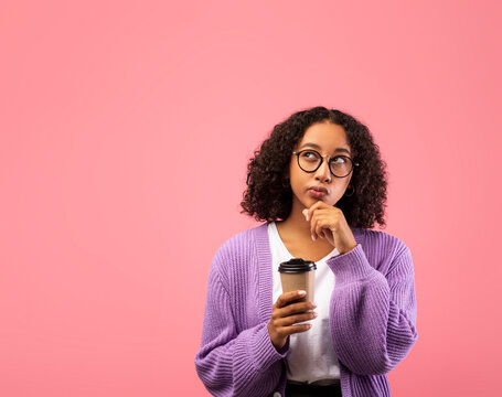 A thoughtful millennial African American female holds a takeaway coffee, gazing into empty space while pondering over an unusual offer.