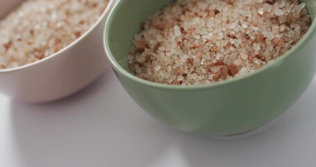 Displaying green ceramic bowl holding coarse pink salt on white table, with peach bowl © vectorfusionart