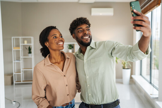 Happy black couple taking selfie using smart phone at home