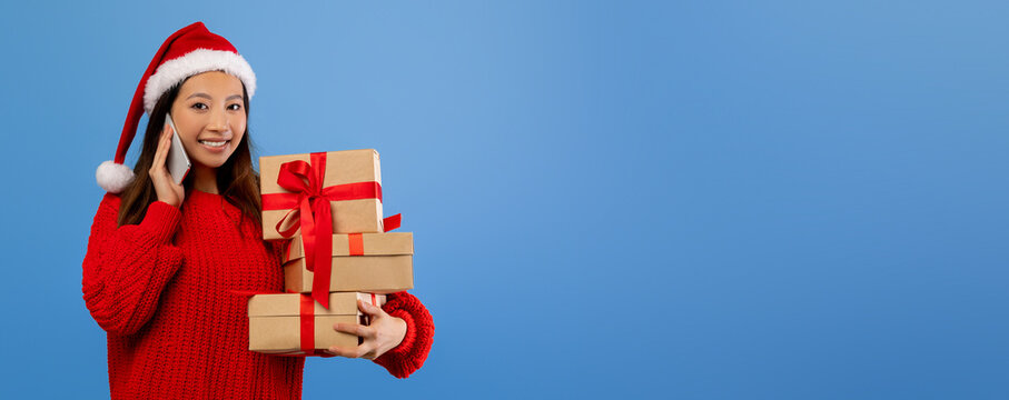 A cheerful young woman in a bright red sweater and Santa hat holds several beautifully wrapped Christmas gifts. She looks excited and happy, embodying the festive spirit.