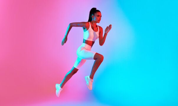An athletic woman is captured mid-run against a backdrop of vibrant pink and blue colors. She wears stylish activewear and displays determination while sprinting.