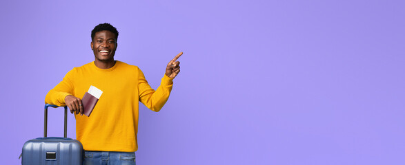 A man wearing a bright yellow sweater is standing near a suitcase. He is smiling broadly and...