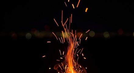 Bright fire sparks flying up at night with dark bokeh.
