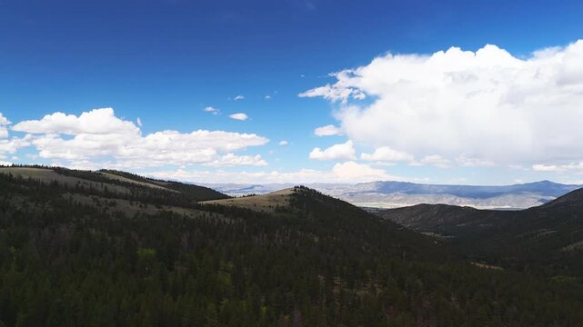 Drone flight over a remote section of the Colorado Rocky Mountains near Poncha Pass, Salida, Colorado with green forests covering the mountains with views stretching to the distance horizon.