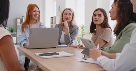 Women group meeting around office table to discuss business tasks and goals. Colleagues share ideas in friendly conversation, work with laptop and tablet, teamwork discussion and team collaboration - Powered by Adobe