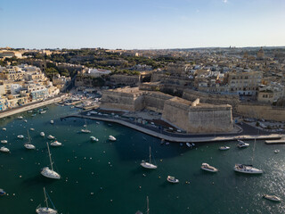 Obraz premium High angle aerial view of traditional boats and luxury yachts in crystal clear turquoise water, scenic Mediterranean coast of Malta, sunny summer travel destination