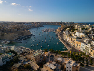 Obraz premium High angle aerial view of traditional boats and luxury yachts in crystal clear turquoise water, scenic Mediterranean coast of Malta, sunny summer travel destination
