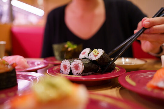 Woman holding Maguro maki sushi with chopsticks in Japanese sushi restaurant.