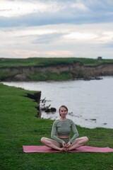 Caucasian woman doing yoga on the river bank. 