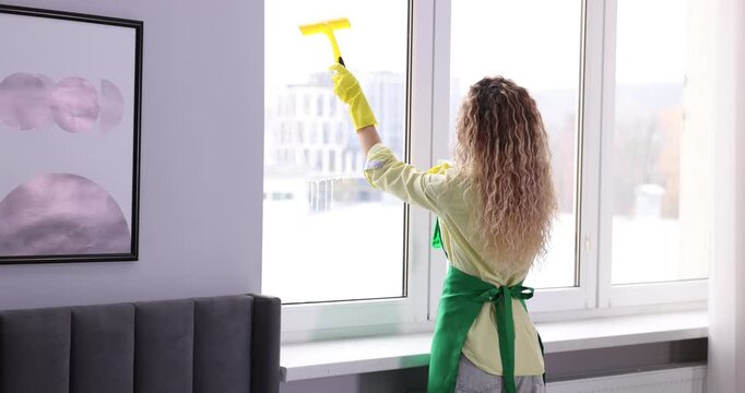Woman cleaning window with squeegee and detergent indoors