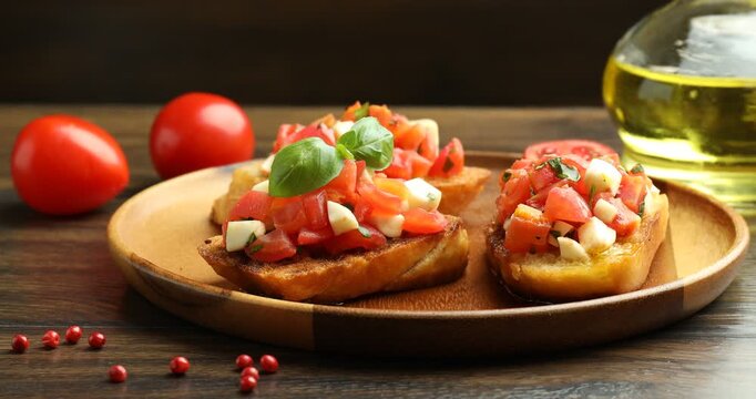 Woman putting basil onto tasty bruschetta with tomatoes and mozzarella cheese at wooden table, closeup