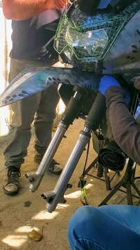 Two riders working on the front forks of Kawasaki KLR650 motorcycle. They are installing a fork brace to upgrade motorbike
