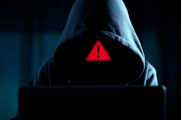 Digital Intruder: A hooded figure, shrouded in shadow, works behind a glowing laptop screen. The image suggests digital danger, hinting at cybercrime and online threats. 