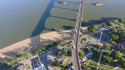 Aerial drone shot of traffic on a major bridge spanning the Paraná River with Corrientes cityscape and surrounding developments visible.