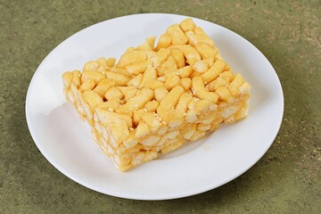A golden-colored sachima piece placed neatly on a round white plate, showing crispy texture and sweet coating.