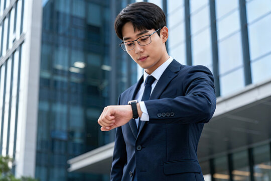 A young businessman in a suit checks the time on his smartwatch outdoors in an urban setting.