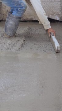 Construction worker using an aluminum straight edge to smooth and level a fresh cement surface, concrete work