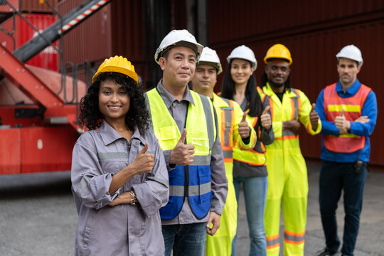 Group of diverse industrial workers giving thumbs up at container shipping yard, expressing success, teamwork and confidence in logistics, supply chain and safe working environments. - Powered by Adobe