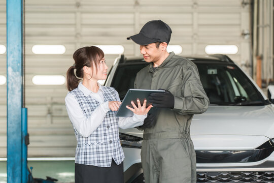 Male and female employees looking at a tablet in the pit of a repair shop (auto repair shop, private vehicle inspection center, staff)
