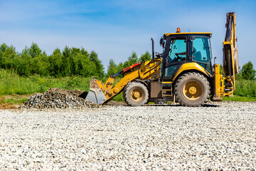 Heavy equipment with front bucket actively moves aggregate material to level ground surface under clear blue sky, selective focus