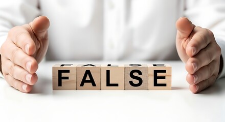Wooden blocks spell false protected by hands on a white surface