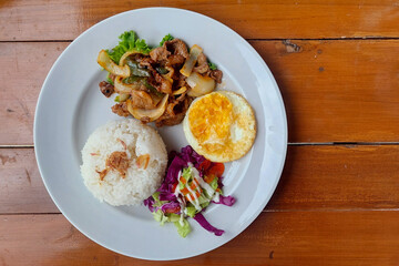 Plate of Beef Stir-Fry, White Rice, Fried Egg, and Salad on a Wooden Table.