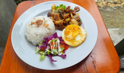 Plate of Beef Stir-Fry, White Rice, Fried Egg, and Salad on a Wooden Table.