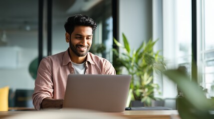 Smiling indian business man working on laptop at home office. Young indian student or remote teacher using computer remote studying, virtual training, watching online education webinar at home office