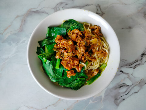 A bowl of traditional Indonesian chicken noodles or Mie Ayam with green vegetables.