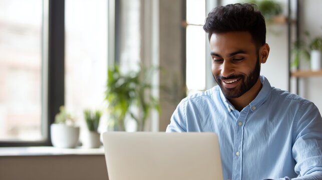 Smiling indian business man working on laptop at home office. Young indian student or remote teacher using computer remote studying, virtual training, watching online education webinar at home office