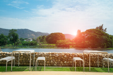 White bench and table with stone wall  on the green grass field near the river. Seat for rest and see view of mangroves forest background 