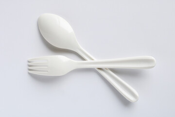 A clean white plastic spoon and fork, arranged on a simple white background, representing basic eating utensils.
