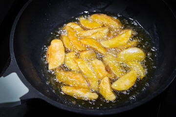 A view of golden potato wedges sizzling and bubbling in hot oil on a frying pan, showcasing the active deep frying process. Cooking this snack or side dish in a kitchen or restaurant setting.