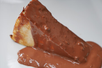 A slice of cheese cake topped with rich chocolate sauce.