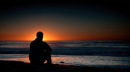 A person sitting on a beach at sunset, gazing out at the ocean.