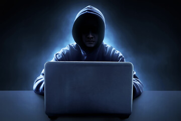 Hacker in hoodie using  laptop on dark background