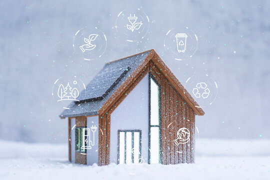 Miniature eco-friendly house model with solar panels surrounded by sustainability and recycling icons on a snowy background. Concept of green energy and smart home technology.