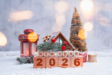 New Year festive composition with wooden cubes and New Year 2026 inscription. Christmas decorations, pine branches and snow. Winter background with lantern light and decorative house.
