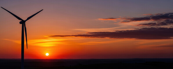 A wind turbine against a vibrant sunset sky with orange and pink hues.