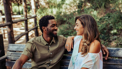 Smiling man and woman sitting close together on wooden bench in nature, enjoying relaxed and happy moment outdoors, surrounded by greenery and sunlight