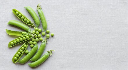 A top down view of several green pea pods and loose peas on a light gray textured surface area space