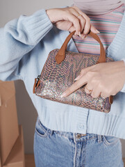 Young woman's body in a knitted sweater and jeans, her hand showing a beautiful snakeskin bag