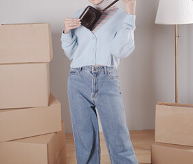 The body of a young woman in a knitted sweater and jeans and her hand shows an elegant shiny dark brown leather purse.