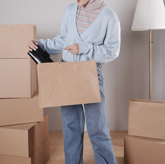 Young woman's body in knitted sweater and jeans putting black leather purse into jumbo paper shopping bag