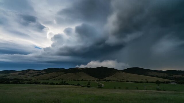 Dramatic storm clouds gather over rolling green hills and a vast field under a moody sky.