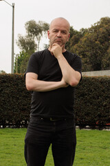 Thoughtful bald man standing outdoors with hand on chin